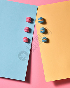 在粉红色纸面背景的蓝和黄纸板上排成一行展示的新多彩色红心面包圈上有阴影的反射顶部视图在多色纸板的粉和蓝红的心面包圈上有粉红色背景图片