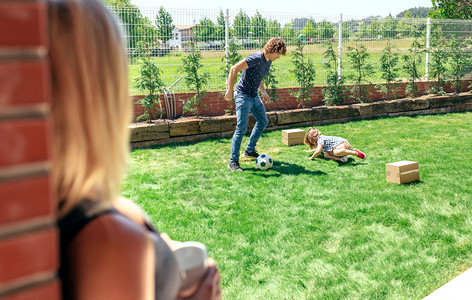 母亲看她的丈夫和儿子在花园踢足球图片