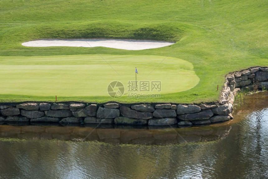 豪华高尔夫球场上的旗子和洞果岭周围有水障碍和沙坑豪华高尔夫球场水沙挑战洞图片