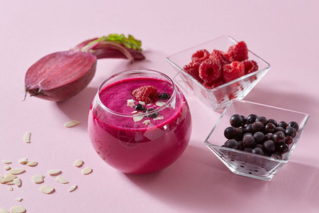 来自红莓和甜菜根的素食健康甜点粉红色纸面的玻璃杯上装着杏仁板红莓的香味半个甜菜草莓和粉红色纸面的黑草莓背景图片