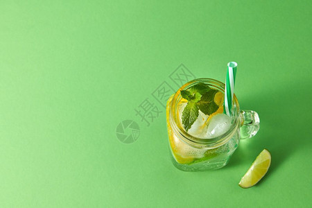 绿色背景的含酒精鸡尾玻璃罐顶部柠檬和冰水玻璃中的塑料吸管等柑橘水果片冷酒精或非夏季饮料的概念由天然柑橘水果自制的冷酒精莫吉托绿色图片