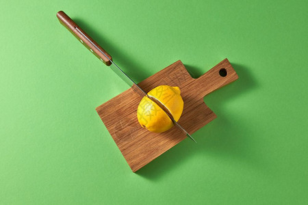绿色背景的柑橘水果黄熟柠檬的顶部视图在木板上两半的黄熟柠檬带有复制空间一把锋利的钢刀用黄熟柠檬切开一把锋利的钢刀用黄色有机柠檬切图片