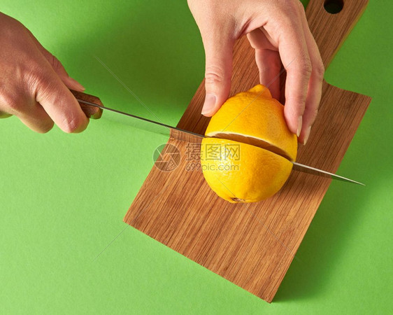 女手的顶部切开一个黄熟柠檬用于在绿色背景的木板上准备天然饮食料健康物概念女孩和一只手在绿色背景的木板上切开半个黄熟柠檬从上面看图片