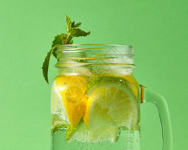 绿色薄荷和天然柠檬石灰的柑橘水果切片玻璃罐中的冰块和天然鸡尾酒绿色背景的泡绿色背景的薄荷糖用天然有机成分制的自饮料中绿色薄荷背景图片