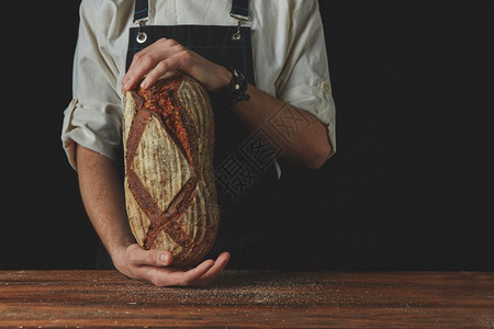 男人和在背景上握着新鲜温暖面包的手吨位照片面包师和手握着奥瓦尔面包图片
