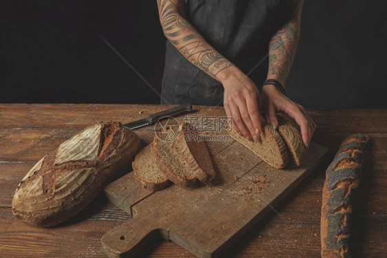 女人手里有新鲜的面包片旧木头背景上有纹身在板上切面包图片