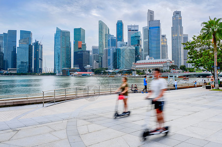 与摩天大楼一起的现代唱诗歌天际线人们在城市堤岸骑着脚踏车图片