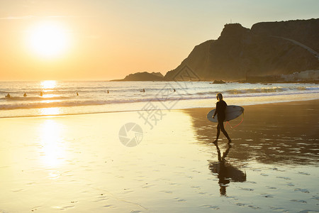 日落时在海滩上行走的有冲浪板女子背影图片