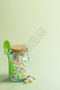 装满各种彩色小棉花糖的玻璃瓶和配着绿勺子的最小图像图片