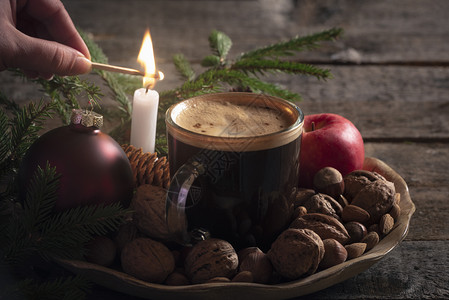圣诞节气氛舒适一个女人点燃蜡烛在一块木板上满了坚果苹和一杯咖啡在低光图片