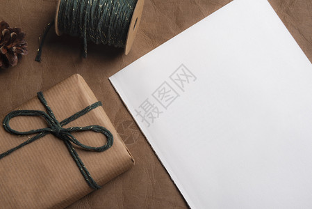 包装在经典棕色纸上的礼品盒面绑有绿色和金的绳子还有一份皮革背景上的未写白纸图片
