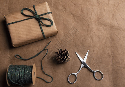 包装礼物的概念包裹在棕色经典纸一个绿色的球和剪刀在棕色皮革背景图片