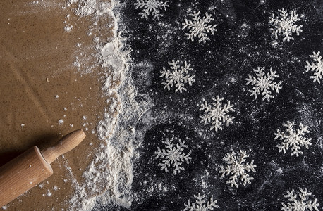 在木制厨房桌上的高角视图面有许多由白粉和滚姜饼棒制成的雪花形状图片