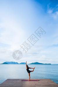 年轻女子在海边的木头码做瑜伽在夏日晴朗的天晴朗在科汉塔克拉比泰兰图片