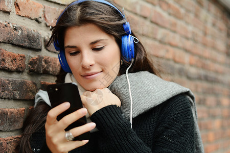 美丽的年轻女子聆听音乐并使用她的智能手机技术概念图片
