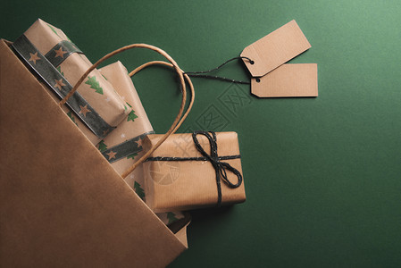 满礼物的棕色纸袋有两个空标签被推翻在绿色背景上传播经典纸包着的礼物图片