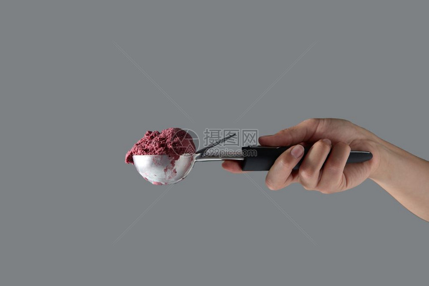 冰淇淋的金属勺子中自制的红莓甜点上面有女人和手放在灰色背景上文字空间一只雌手在灰色背景的勺子上拿着甜冷红樱桃冰淇淋夏天有复制空间图片