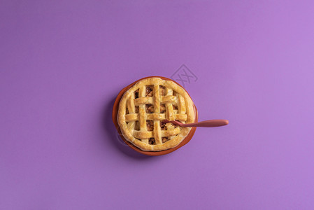 一个苹果馅饼的顶部在一个生锈的瓷器盘里面有一个茶匙紫色背景准备吃甜点平坦的躺下最起码风格图片