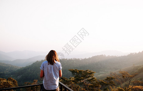 欢喜地庆成功的女人在日落或出站在山顶仰望美丽的山峰图片