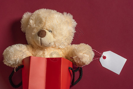 红纸袋里的泰迪熊玩具上面印着空白标签红纸背景圣诞礼物购黑色星期五销售图片