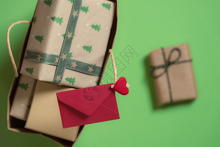 装满礼品盒的袋和贴在手柄上的红色信封以及一份绿色背景的单独礼物xma礼物和信件图片