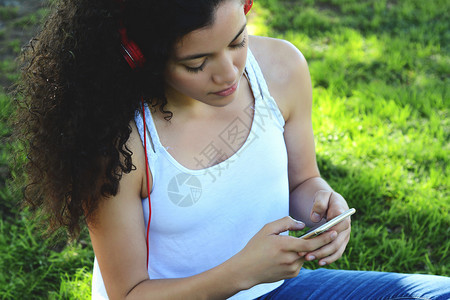 美丽的年轻女子坐在草地上用智能手机发信息图片