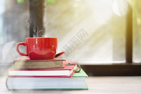 红咖啡杯上面有烟雾在堆叠的旧书上放在木板有窗户灯光圣诞快乐概念背景休息或阅读图片