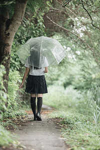 下雨时在自然行走道上带着雨伞行走的亚裔女学生肖像图片