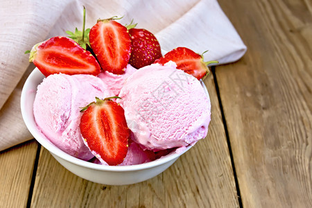 白碗中的冰淇淋草莓浆果餐巾纸在旧木板的背景上图片