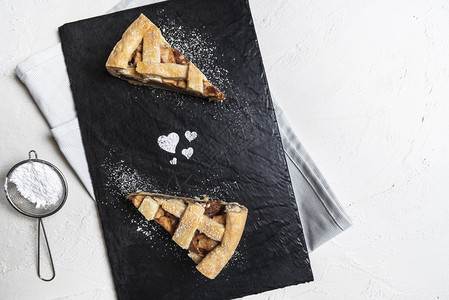 上方有两块苹果派切片在削板上心形来自糖粉和筛子在厨房桌上情人节甜点图片