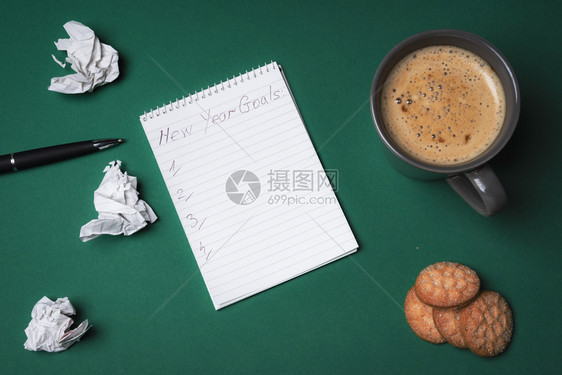 有新年目标空白清单的螺旋笔记本周围环绕着折叠页一杯咖啡和甜饼干设定目标概念图片