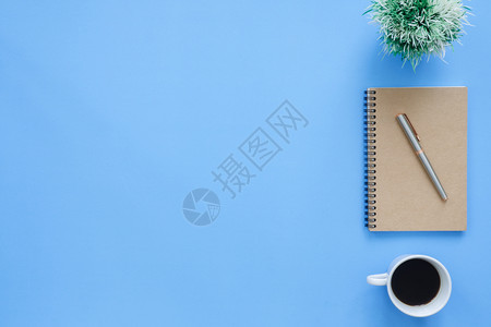 办公桌工作空间平面的一张工作空间模拟照片上面有咖啡杯笔记本和蓝面糊背景的装饰品图片