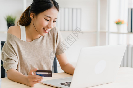 使用计算机或笔记本电脑购买信用卡在线物同时穿着毛衣坐在家中客厅的办公桌上图片