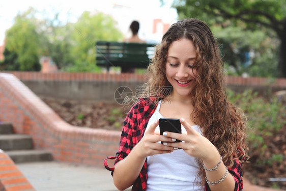 美丽的年轻女子在街上用智能手机发信息图片