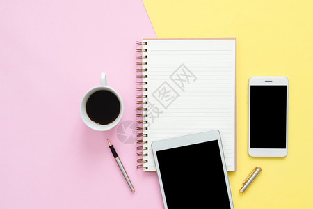 办公桌工作空间平坦地铺设工作空间的顶层视图上面有空白笔记本页咖啡杯和糊面背景的电话平板粉色彩背景空间概念图片