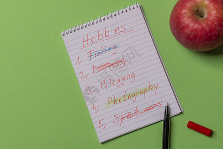 手写在螺旋笔记本上的爱好列表和绿色彩背景上的红苹果直接在视图上方复制空间图片