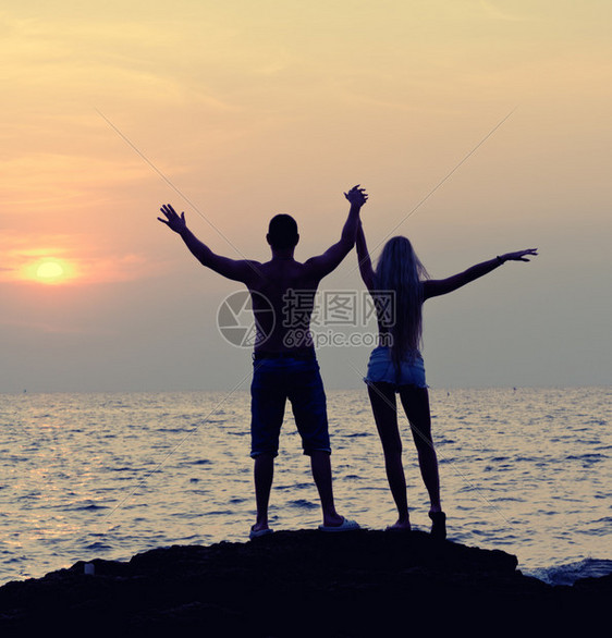 年轻快乐的男女青年休眠日落时在海滩上举起手图片
