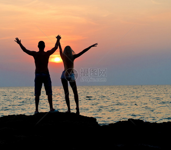 年轻快乐的男女青年休眠日落时在海滩上举起手图片