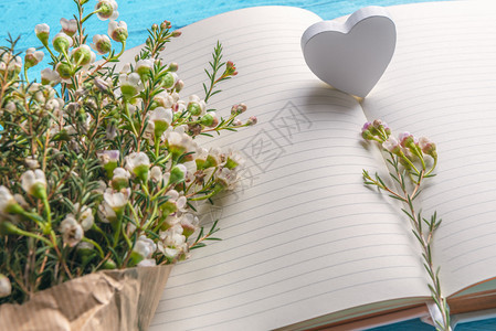白小花和木心写在空白笔记本页上蓝背景特写情人节框架婚礼计划背景图片
