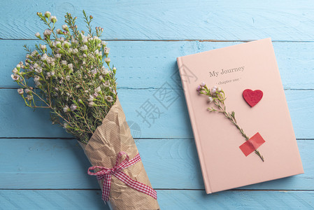 粉红色笔记本和美丽的春花束放在蓝色木制桌子上图片