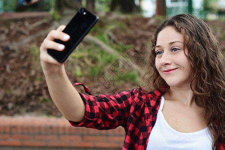 一位年轻美女用智能手机拍自的肖像户外图片