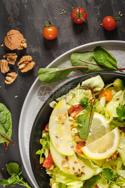 新鲜蔬菜沙拉加番茄苹果坚种子和柠檬橄榄油倒入沙拉碗图片