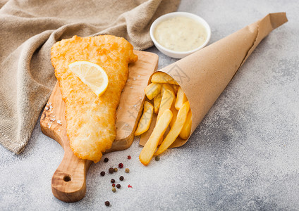 传统的英国鱼和薯片在白桌背景的切肉板上加塔酱图片
