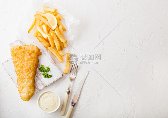 传统英国鱼和薯片在切肉板上加塔酱叉子和刀白石桌底面加柠檬片图片