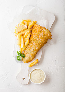 传统的英国鱼和薯片在白桌背景的切肉板上加塔酱图片
