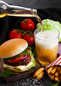 新鲜牛肉汉堡配有酱汁和蔬菜啤酒杯薯条在石器厨房背景图片