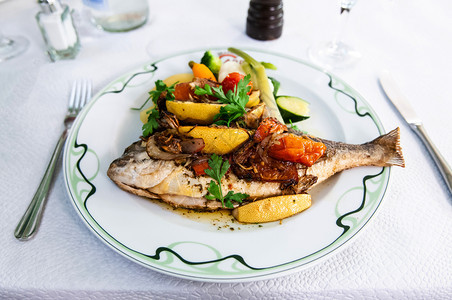 盘子鱼餐桌上加烤鱼和蔬菜番茄Zuchin胡萝卜和柠檬的烤鱼图片
