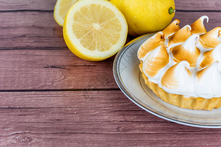 新鲜自制柠檬派配有蛋白糖和木制桌上的柠檬柑橘水果图片
