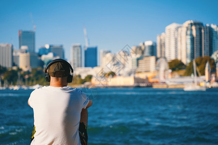 一个人坐在海滩上听着音乐和城市风景在他面前生活方式的概念图片