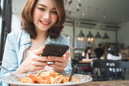 一位年轻女子在智能手机上拍摄意大利面条食品图片